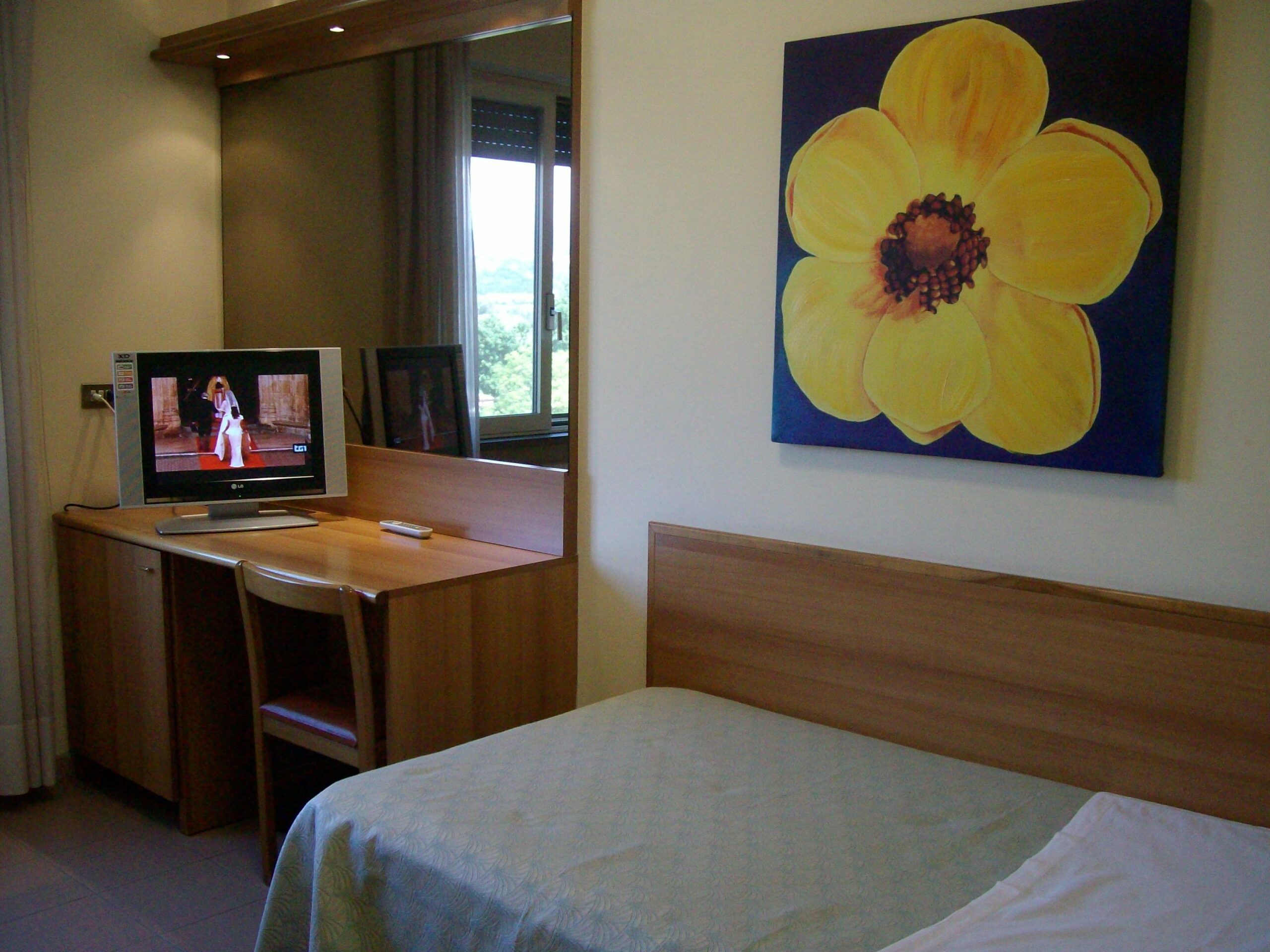 Una camera con letto, scrivania, televisore e quadro colorato