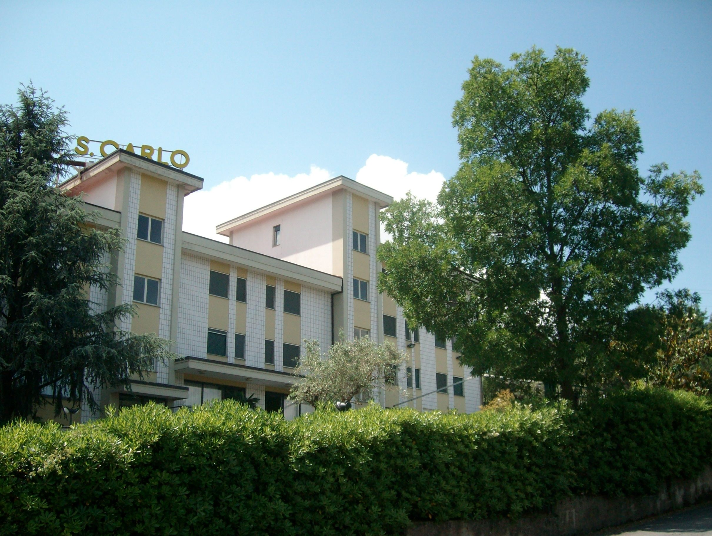 La facciata di Villa San Carlo tra gli alberi, con l'insegna sul tetto