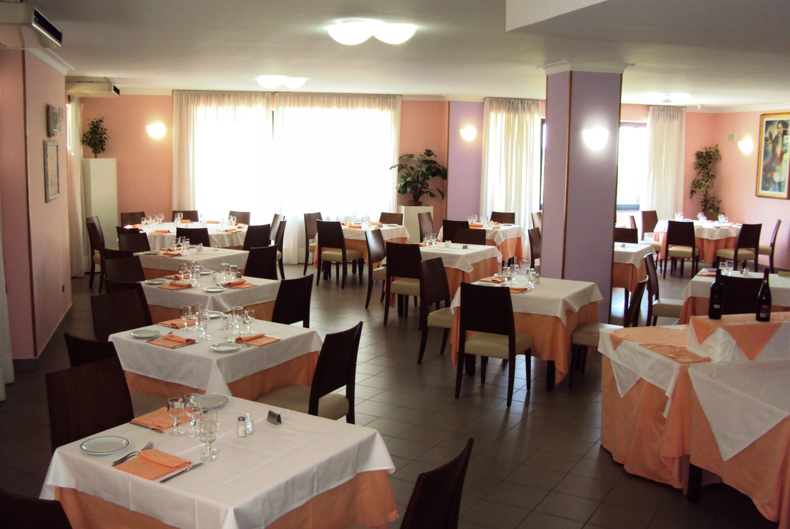 La sala da pranzo con tavoli apparecchiati e grandi finestre